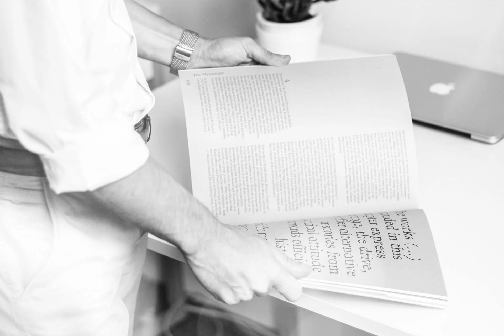 chwarz-weißes Foto einer Person beim Lesen eines geöffneten Buches.